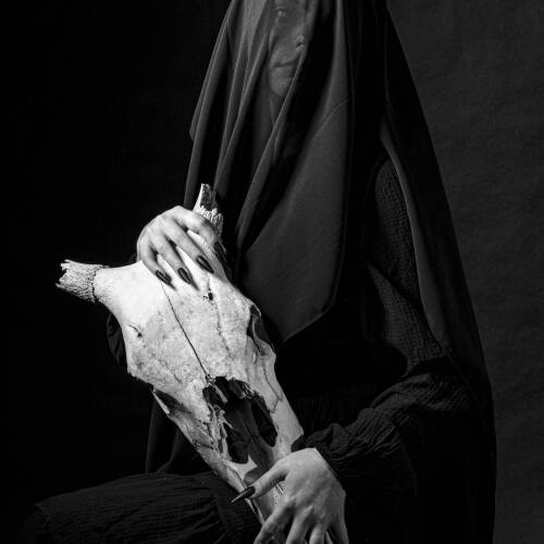 Black and white photograph of a person covered in black fabric holding a skull.